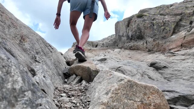 Determined female hiker with a backpack scrambling up a steep and challenging rocky mountain path, displaying a strong spirit of adventure and perseverance on her ascent