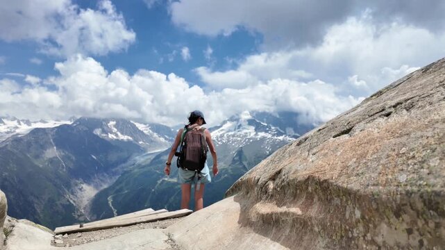 Adventurous female hiker with a backpack enjoying the panoramic view of the majestic mont blanc massif and the mer de glace glacier from a scenic overlook in the french alps