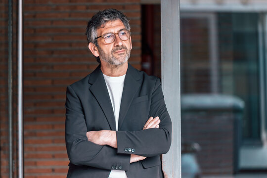 Smart mature businessman posing to camera while standing in front of the office