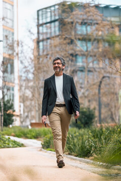 Happy mature businessman using his phone while walking through the park