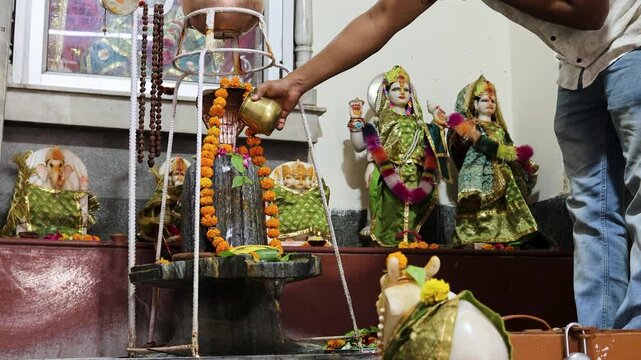 hindu devotee performing shivling abhishek ritual inside indian temple with sacred offerings