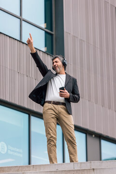 Funny businessman dancing and listening to music with headphones in front of the office.