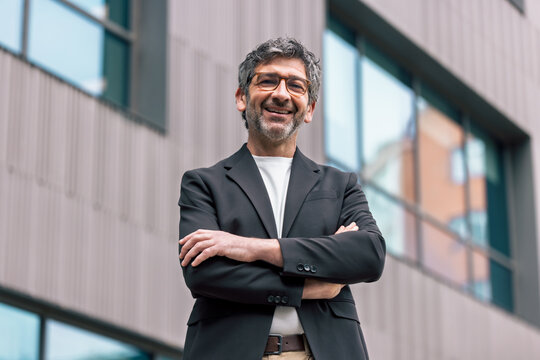 Smart mature businessman posing to camera while standing in front of the office