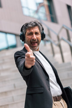 Funny businessman dancing and listening to music with headphones in front of the office.
