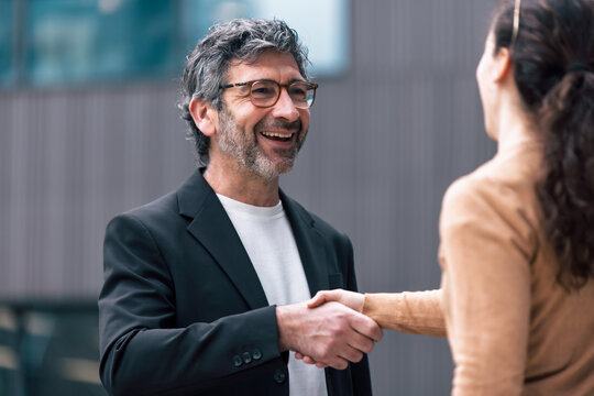 Elegant businessman shaking hands while talking with a woman in front of the office.
