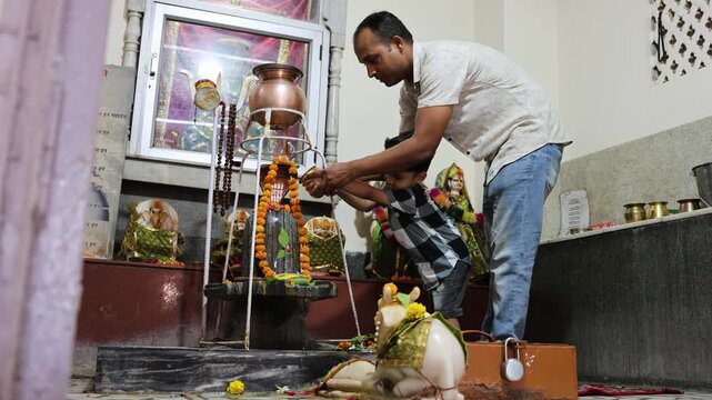 father helping young child perform shivling worship inside hindu temple shrine