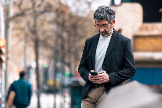 Mature elegant businessman using smartphone while walking through the city.