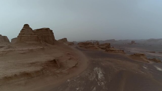 Yardang rocks with visible tracks in desert under hazy sky creating natural erosion landscape with human trace perfect for geology and adventure stock video footage.