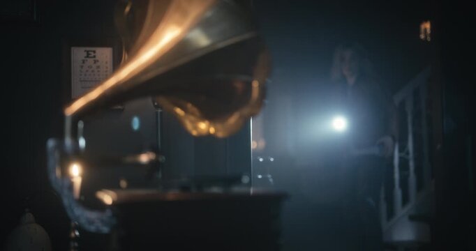 As woman with flashlight turns to face gramophone, a record turns on it&rsquo;s turntable