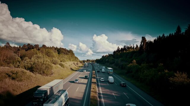 A high-angle view of a highway cutting through a green landscape where one side is congested with a long line of cars and trucks, while the other side flows freely under a cloudy sky.