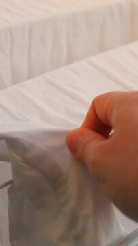 Outdoor drying white sheets hands arranging on rack, rows of fabric fluttering in breeze, closeup fingers tugging corner, summer sunlight, backyard chore by homemaker, rhythm of household maintenance,