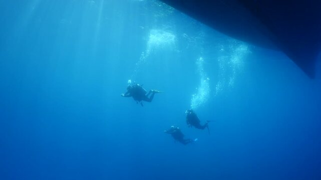 scuba diver scenery under the parked boats with sun beams and rays underwater