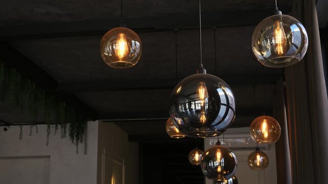 Spherical glass pendant lights glow softly while hanging from a dark ceiling in a modern cafe setting. Concept of cozy interior design and welcoming restaurant atmosphere.