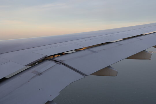 Airplane wing spoilers deployed above the sea during sunset.
