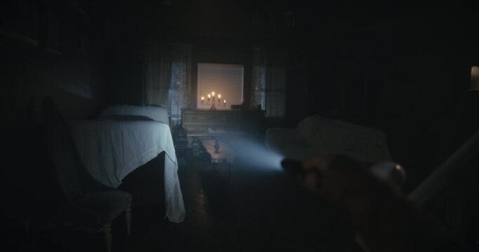 Point of view of woman aiming small flashlight into dark, scary looking living room at night