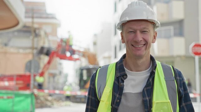 Man builder smiling in hardhat and high visibility vest on street construction site with excavator and rubble; pride responsibility.
