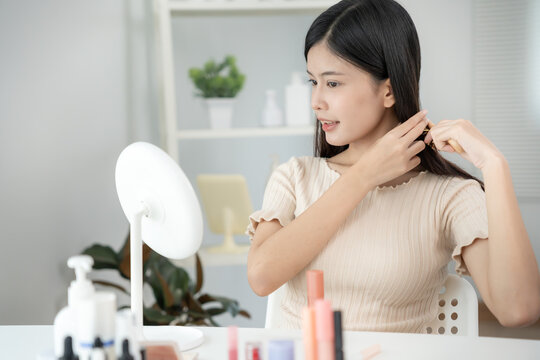 Beautiful Asian woman sit in front of a mirror and comp my hair. face of a healthy woman applying makeup. Advertisement, lifestyle , cosmetics, makeup accessories, beauty activity, beautician