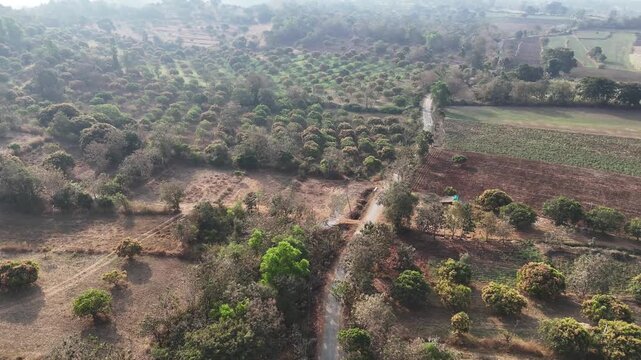 Cinematic aerial view of the rural landscapes near Mollem featuring patchwork farmlands, winding dirt roads, and dense tree cover stretching across dry countryside terrain.