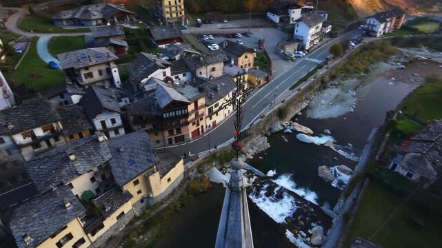 Drone orbiting around bell tower of church in alpine village of Fontainemor, Lys river at dusk in Aosta Valley, Italy