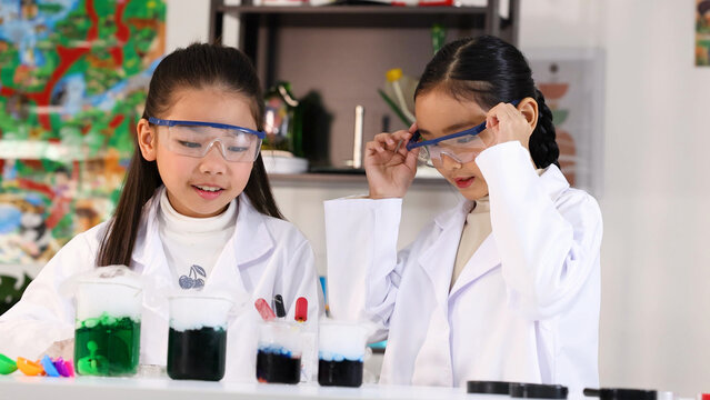 Two Young Asian Girls in Lab Coats Conducting Science Experiments with Beakers