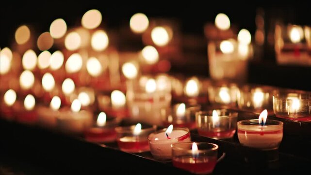 Rows of lit vigil candles flicker gently in darkness creating atmosphere and ambiance for prayer and reflection.