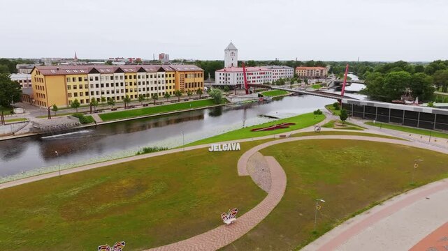 Establishing shot, visible Jelgava sign beside peaceful urban waterfront area