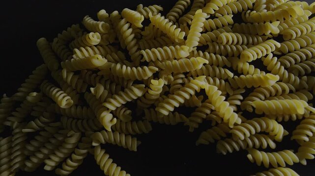 50p top view macro slider shot moving above uncooked fusilli pasta.