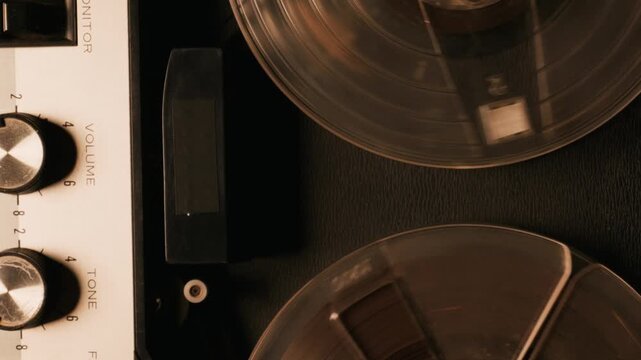 Vintage reel tape recorder spinning its transparent reels with warm nostalgic lighting over dark texture. Concept of classic analog audio technology and retro music recording history.