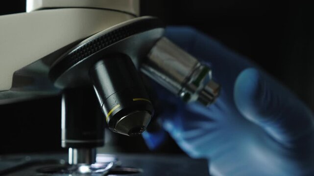 Scientist hand in blue glove rotates microscope objective lens for examination.