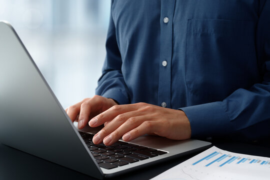 Businessman using laptop computer at desk in office. Closeup of hands and keyboard. Business technologies.
