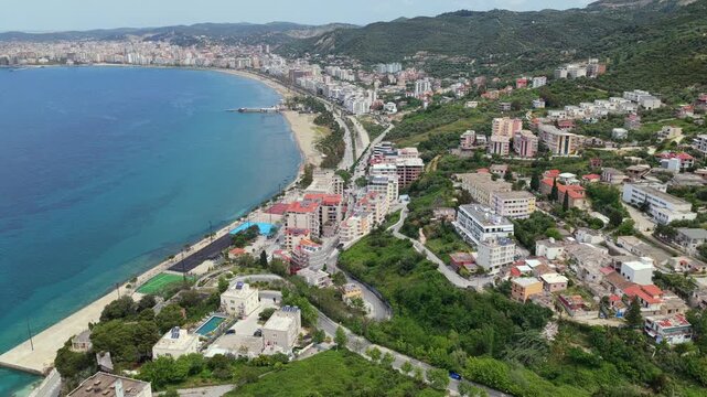 Aerial video overlooking the grand crescent bay of Vlora, Albania, highlighting red-roofed hillside houses and neighbourhoods nestled on green slopes.