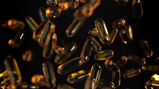 Golden softgel capsules fall against black, glossy omega oil pearls Filmed on a high-speed camera at 1000 fps.