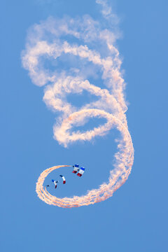 Paratroopers diving with French tricolor parachutes and smoke trails in blue sky