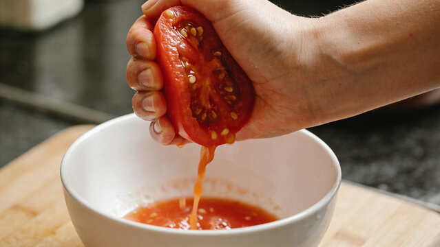 Squeezing a ripe tomato into a bowl in a kitchen setting for fresh cooking