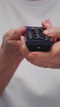 Remote control is in old hands. Old man or elderly woman turns on an old TV and holds the remote control in his palms. Retro viewer presses the buttons on the control panel. Switching channels. Key