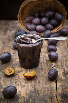 Preserving jar of plum jam and plums on wooden table