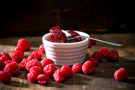 Bowl of raspberry jam, spoon and raspberries on wooden table