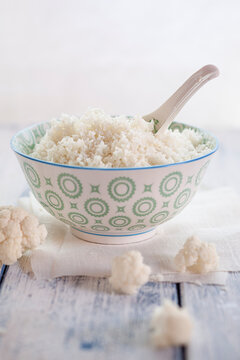 Bowl of cauliflower rice and cauliflower florets on cloth and wood
