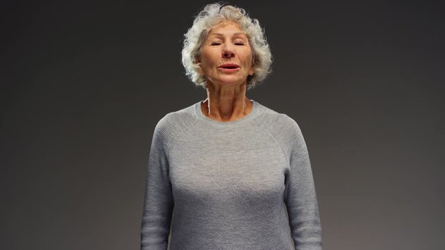 Portrait: senior gray haired woman relaxing, take a deep breath. Retired female breathing deeply, smiling looking at camera. Mature old female enjoys air. Healthy calm nervous system, well-developed