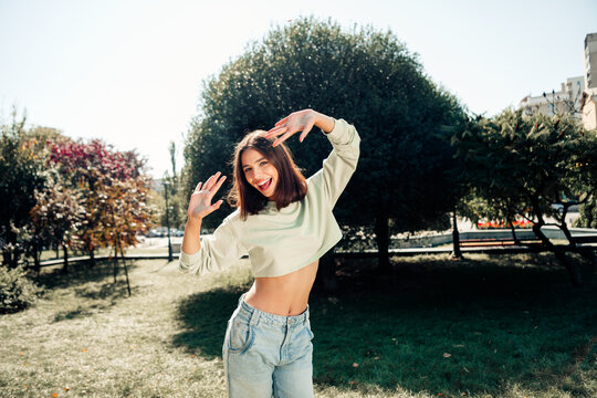 Happy young woman dancing in sunny park wearing crop top and jeans, carefree outdoor portrait of youth and joy