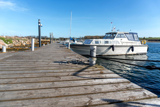 White cabin motorboat is tied to a weathered wooden dock with ropes and fenders on blue lake water, creating a clean marina scene for boating, sailing, and summer travel use.