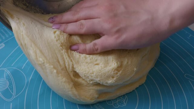 Close-up of fresh raw yeast dough with elastic texture being placed onto a blue silicone pastry mat with measurements. Concept of home baking, pastry preparation, and artisanal bread making.
