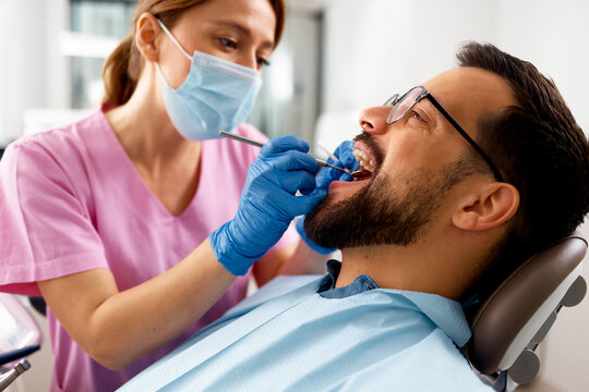 Female dentist examining male patient teeth during dental appointment