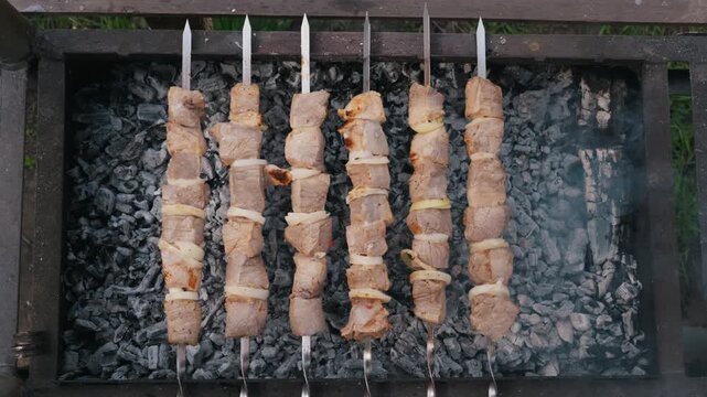 Six skewers of marinated pork meat and onions cook over hot glowing embers in a metal grill. Concept of summer picnic, traditional outdoor barbecue, and savory meat preparation.