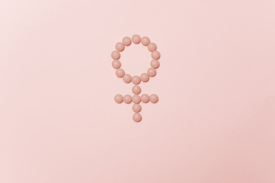 Female gender symbol made from pink pills on pastel background for women health concept copy space