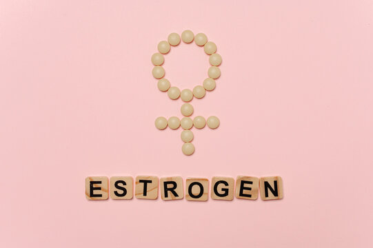 Estrogen word with female symbol made from pills on pastel pink healthcare background