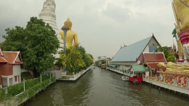 The video frame captures a distinct perspective from a bridge overlooking Khlong Phasi Charoen. The calm waters of the canal stretch down the center, lined with lush green trees, local houses, and tra