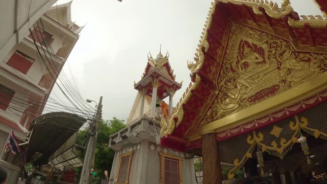 The video footage captures a scene within a temple complex, focusing on a traditional Thai bell tower (Ho Rakhang). A Buddhist monk dressed in bright orange robes is seen standing on the platform.