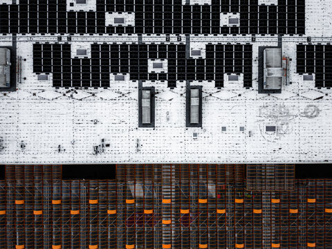 Aerial view of solar panels on a white industrial roof and rows of orange windows Warszawa, Wojewodztwo mazowieckie, Poland.