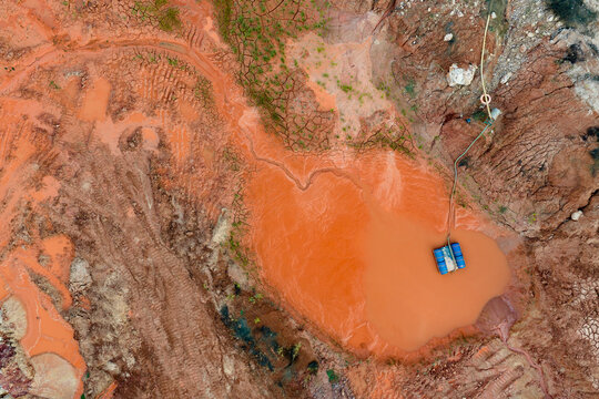 Aerial view of an excavation site with reddish-orange soil and a muddy pool featuring a blue floating pump in Coimbra, Coimbra District, Portugal.